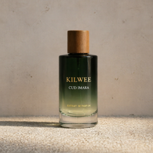 Kilwee perfume bottle with a warm wooden cap, green-to-clear glass, labeled Cud Imara, standing on a textured beige surface.