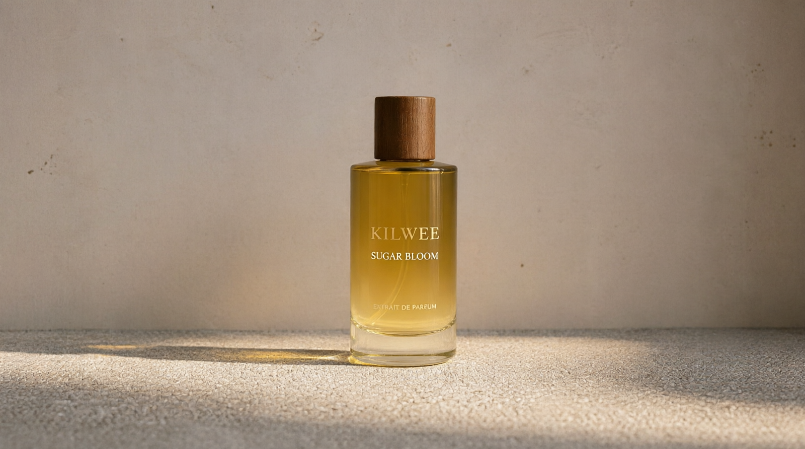 Perfume bottle with a wooden cap labeled KILWEE SUGAR BLOOM on a textured beige surface under warm light.